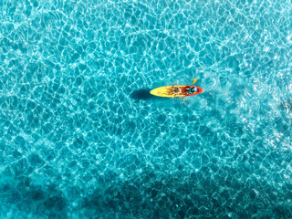 Aerial view of a kayakers paddling through vibrant turquoise shallow waters in deep blue ocean, creating a breathtaking contrast and showcasing the beauty of a tropical paradise. Top view of canoe