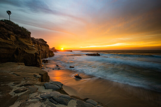 Warm glowing sunset in La Jolla San Diego California with ocean waves crashing onto the beach next to cliffs