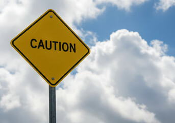 Caution sign against a bright blue sky filled fluffy white clouds