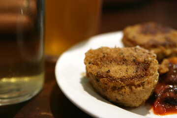 A close-up of a golden-brown, crispy-looking patty on a white plate, served with a dollop of reddish sauce or chutney.