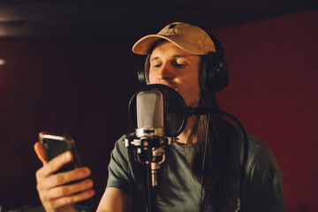 Singer recording song reading lyrics from smartphone in music studio