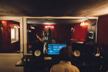 Singer recording song with sound engineer in music studio