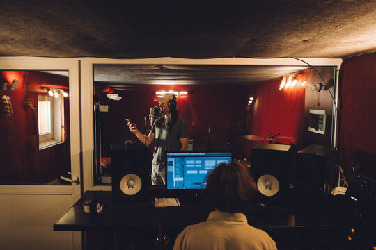 Singer recording song with sound engineer in music studio