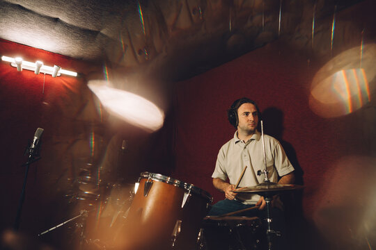 Drummer recording music in professional studio with headphones and drumsticks - Powered by Adobe