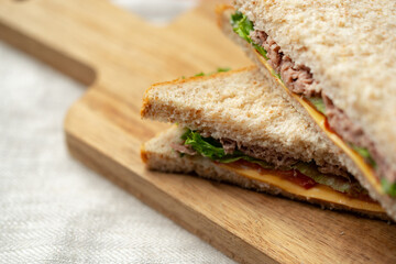 Freshly made sandwich with layers of tuna, lettuce, and cheese on a wooden cutting board at lunchtime