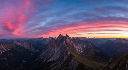 Naklejka premium A breathtaking aerial view of jagged mountain peaks under a vibrant sunset sky with clouds