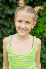 Smiling girl with space buns hairstyle in front of green leaves