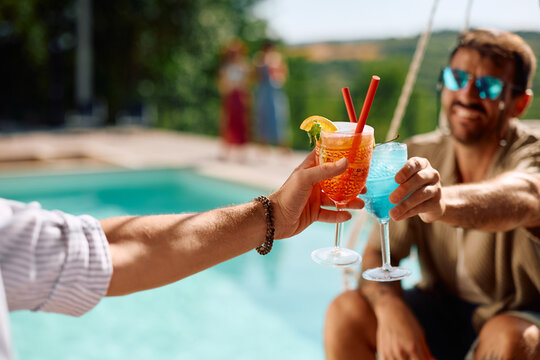 Close up of male friends toasting with cocktails at poolside in summer day.