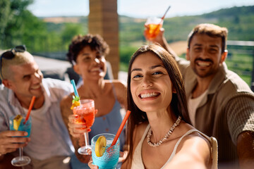 Happy woman and her friends taking selfie while drinking summer cocktails and looking at camera.