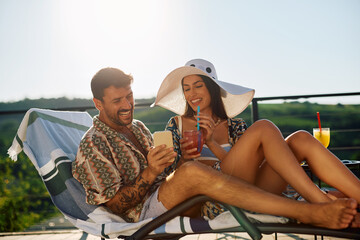 Happy couple using smart phone while drinking summer cocktails on patio.