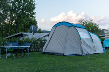 Spacious camping tent set up on green grass with outdoor furniture nearby, surrounded by trees and a serene atmosphere for relaxation and adventure