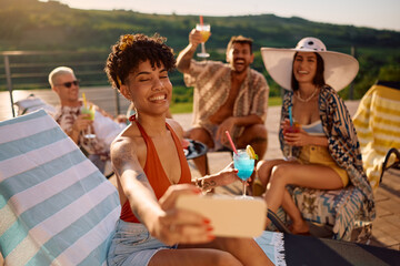 Happy friends having fun in summer while drinking cocktails and taking selfie.