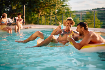 Fototapeta premium Cheerful men laughing while drinking summer cocktail in swimming pool.
