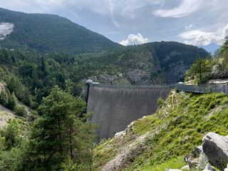 Vajont Dam. Massive concrete dam surrounded by lush green mountains and trees, showcasing...