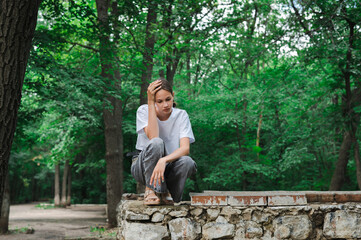 Upset teenager sits on stone fence in abandoned park