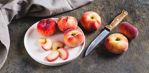 Close up of whole and sliced peaches and a knife are placed on a plate on the table web banner