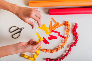 A girl's hands pour glue onto a strip of paper to make a paper chain top view