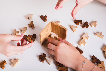 Children's hands assemble a puzzle of wooden figures on the table