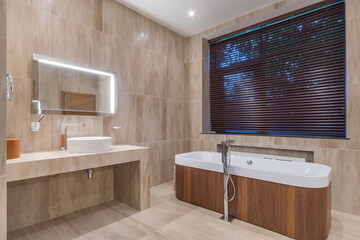 Stylish and concise design of the bathroom, decorated in beige tones, with a bathtub located by the...