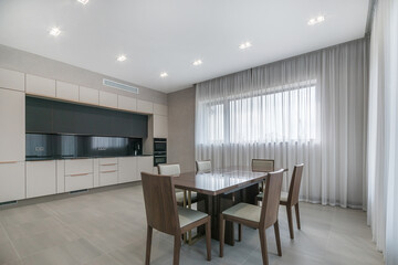 The modern interior of the kitchen is decorated in light neutral tones with a dining table and...