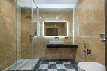 The bathroom is decorated with brown marble tiles, with a modern shower behind a glass partition.