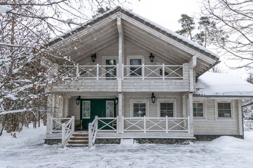 A modern wooden house with balconies and a welcoming porch set against a snowy winter landscape.