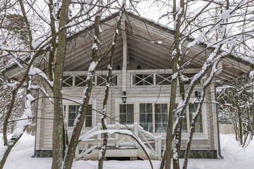 The house is made of wooden beams with a balcony and a porch, surrounded by snow-covered trees on a...