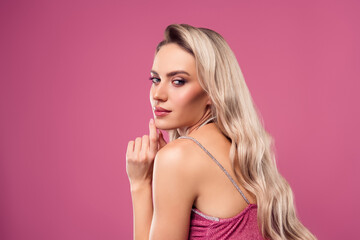 Stunning young woman with flowing blonde hair and stylish makeup posing on vibrant pink background