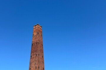 A tall brick chimney rises against a clear, vibrant blue sky.
Concept of: Industrial heritage.
