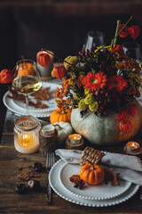 Beautiful elegant table setting for candlelight Thanksgiving Day dinner or Halloween party at home. Fancy dishware, porcelain plates. Floral centrepiece, pumpkins and burning candles as decor