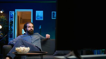 Man entering room, eating popcorn while watching interesting movie on streaming service, enjoying...