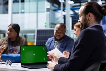 Photovoltaics factory workers analyzing data, reviewing system health metrics with green screen laptop. Solar panels plant employees troubleshooting technical issues using chroma key notebook