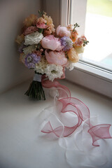 Beautiful floral bouquet with mixed pastel flowers including peonies, roses, and carnations, elegantly arranged with a delicate pink ribbon, set by a window to catch the soft light.