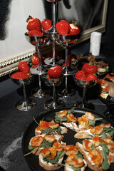  A sophisticated display of fresh strawberries in silver cups alongside shrimp appetizers on a black table. Perfect for gourmet presentations and elegant dining events.