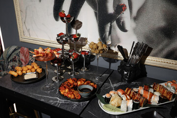 Buffet table beautifully arranged with sushi, tempura, and skewered shrimp. Champagne glasses filled with strawberries add a sophisticated touch to the presentation.