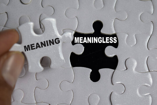 Hand holding piece of jigsaw puzzle with word meaning and meaningless. Business and finance concept