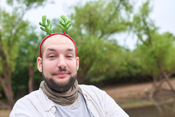 A young Hispanic man wearing a funny Christmas reindeer antler headband smiles amused at the camera...