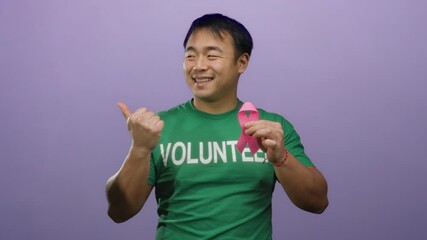 Asian man volunteer holding pink ribbon against purple background promoting breast cancer awareness with a confident smile.