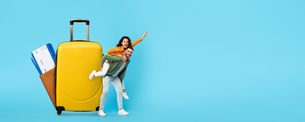 A young couple is joyfully posing with a large yellow suitcase. They plan their summer travels,...