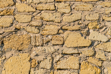 Close-up view of an aged Central European stone village wall, rough texture, gray to brown stones, weathered with discoloration and flaking, natural lighting casting shadows