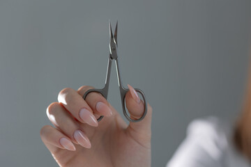 Manicure scissors in hand, close-up. beautiful and elegant manicure in beige tones. beauty salon,...
