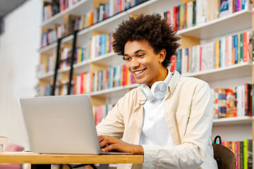 Happy Black male university student preparing for lecture, using laptop while studying in college...