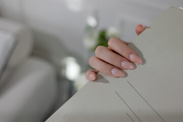 Close-up of elegant beige gel manicure on long almond nails, showcasing feminine glamour.