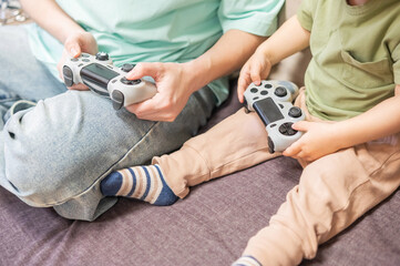 Caucasian woman teaches her little son to play console. Joystick in hands. 