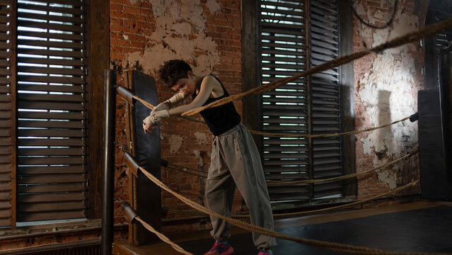 Short-haired boxer resting on ropes between rounds, intense cinematic training moment.
