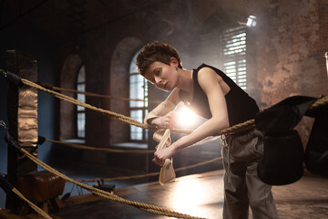 A woman in a boxing gym, portrait by the ropes, cinematic style, dark tones. Training and overcoming oneself, motivation