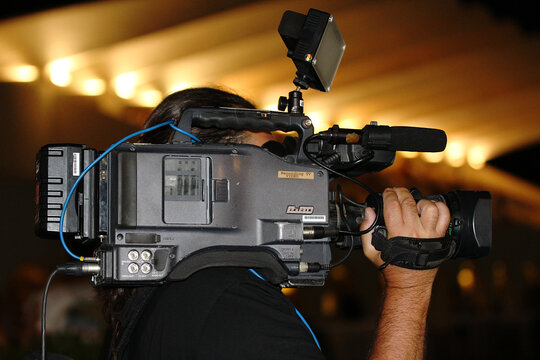 Camar&oacute;grafo nocturno de medio de comunicaci&oacute;n audiovisual TV filmando y enfocando por la noche con c&aacute;mara profesional de v&iacute;deo al hombro  en exteriores