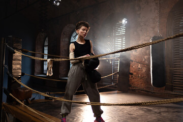 A woman in a boxing gym, portrait by the ropes, cinematic style, dark tones. Training and overcoming oneself, motivation