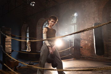 A woman in a boxing gym, portrait by the ropes, cinematic style, dark tones. Training and overcoming oneself, motivation