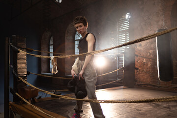 A woman in a boxing ring, holding boxing gloves in her hands, preparing for boxing training. The photo is in a cinematic style, the light gives the mood to a sports motivational story about self